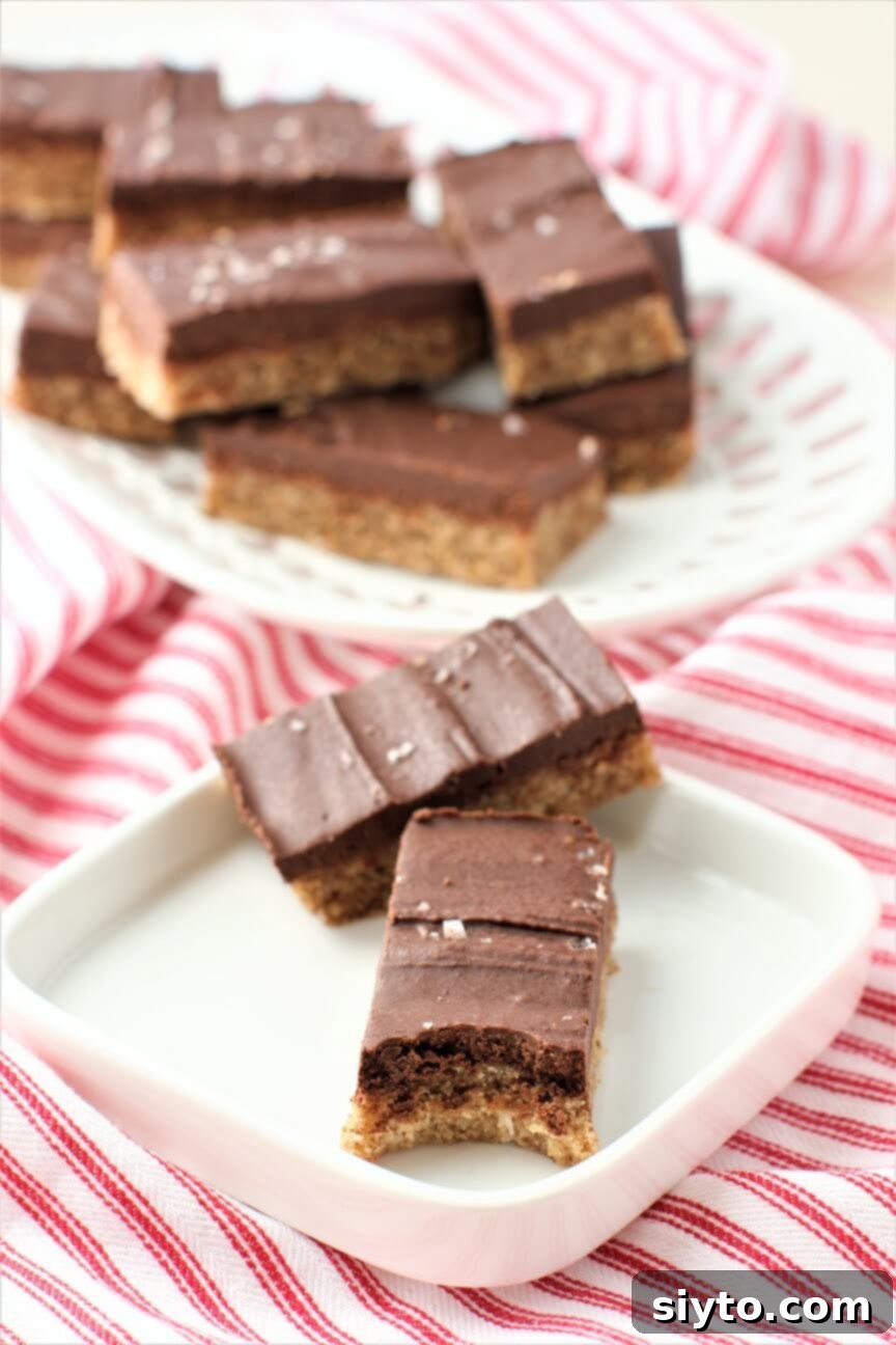 Two No-Bake Chewy Chocolate Almond Bars on a plate, with a bite taken out of one, highlighting its tempting interior.