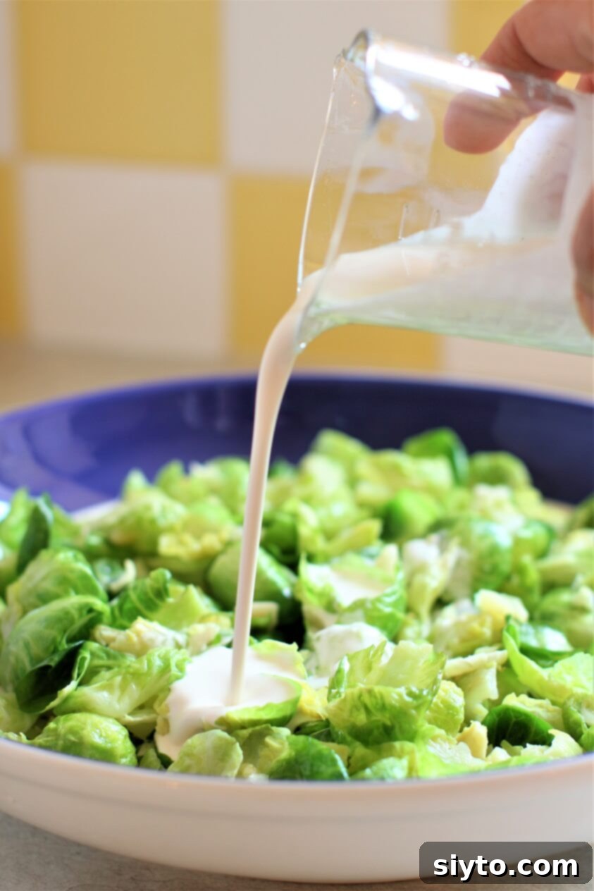 Pouring the creamy, tangy dressing over the warm Brussels sprout leaves in a shallow bowl