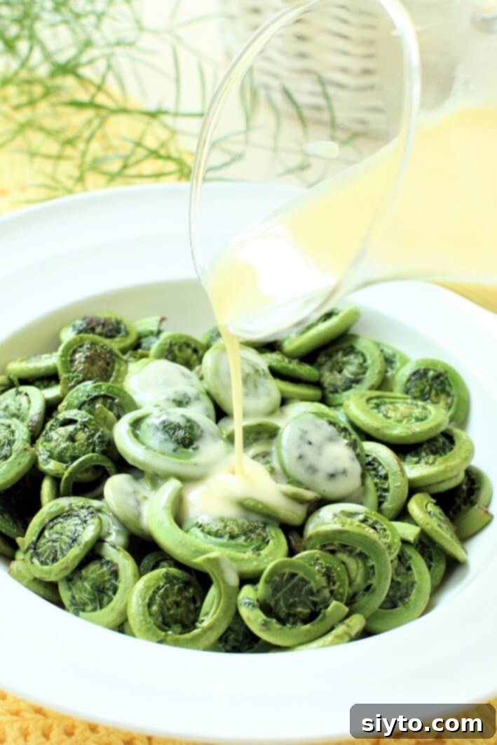 drizzling the butter sauce onto a bowl of cooked fiddlehead ferns