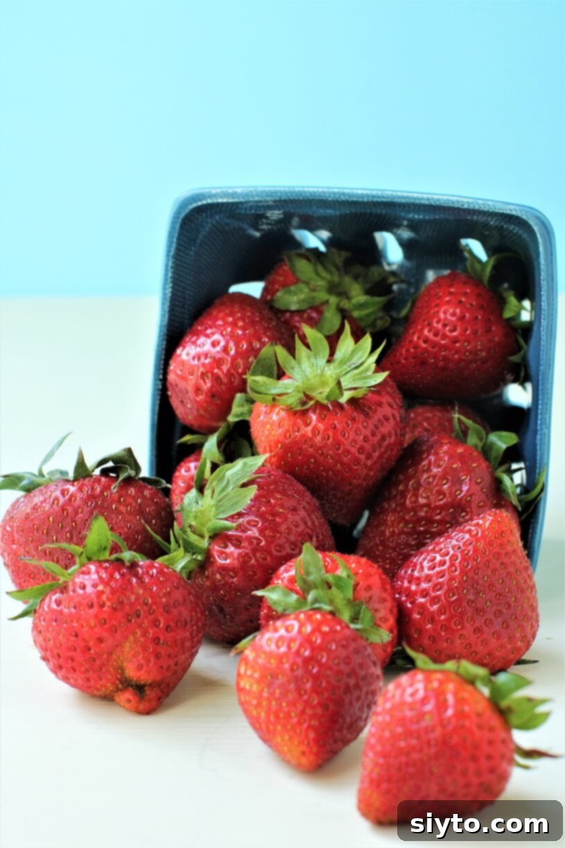 A punnet overflowing with vibrant red, ripe strawberries, some tumbling out enticingly, ready for blending into a refreshing drink.