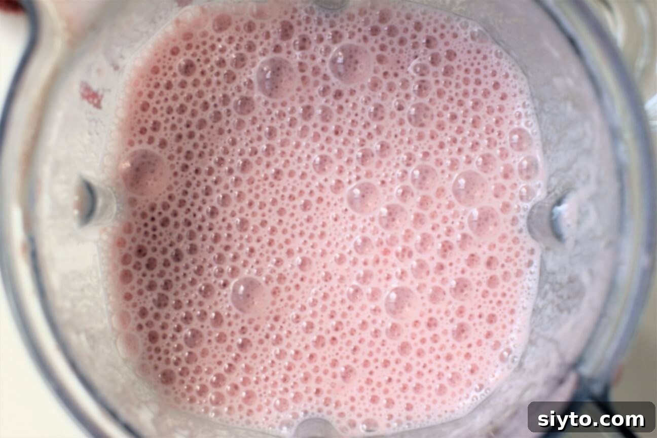 Looking down into a blender, showing frothy, delicate pink bubbles forming as strawberries and milk are blended together.