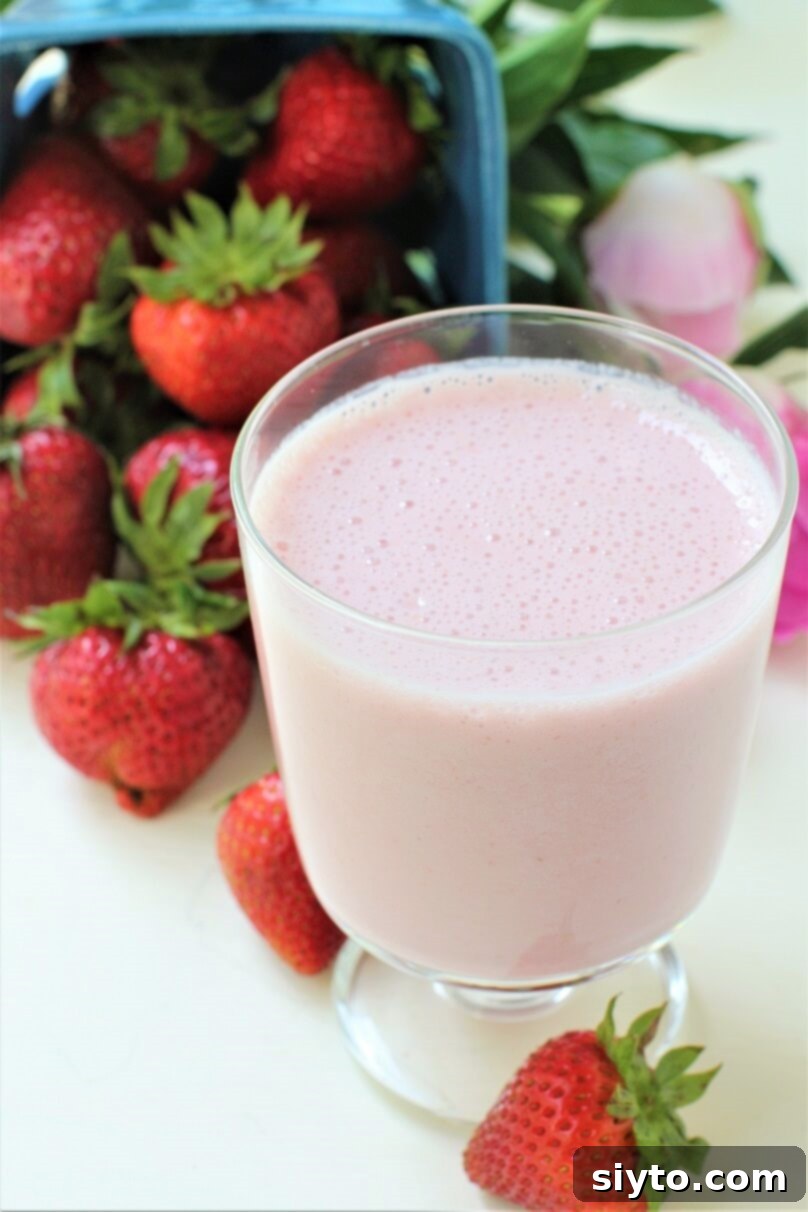 A glass of pink strawberry milk, perfectly chilled, surrounded by a scattering of fresh, whole strawberries on a rustic surface.