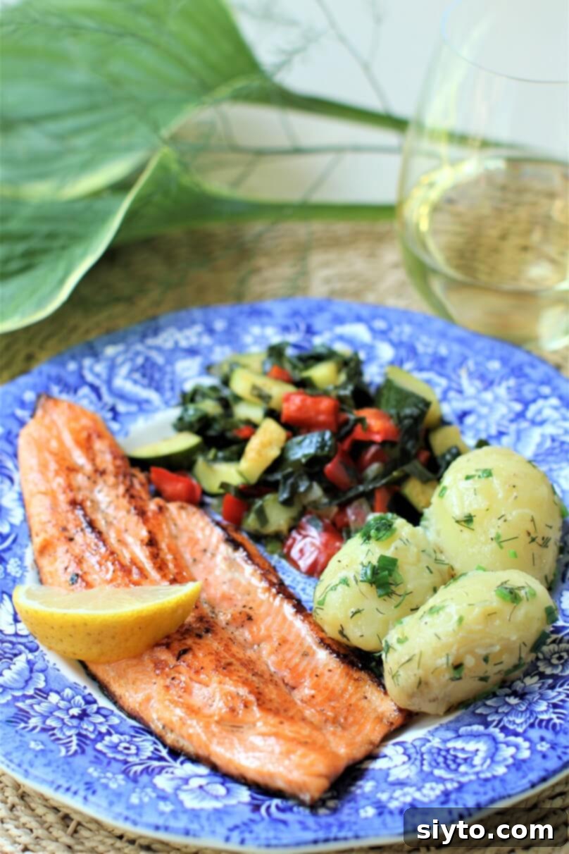 Pan-fried trout fillet on a blue plate, garnished with herbed new potatoes and zucchini-pepper stir-fry, showcasing its golden crispiness