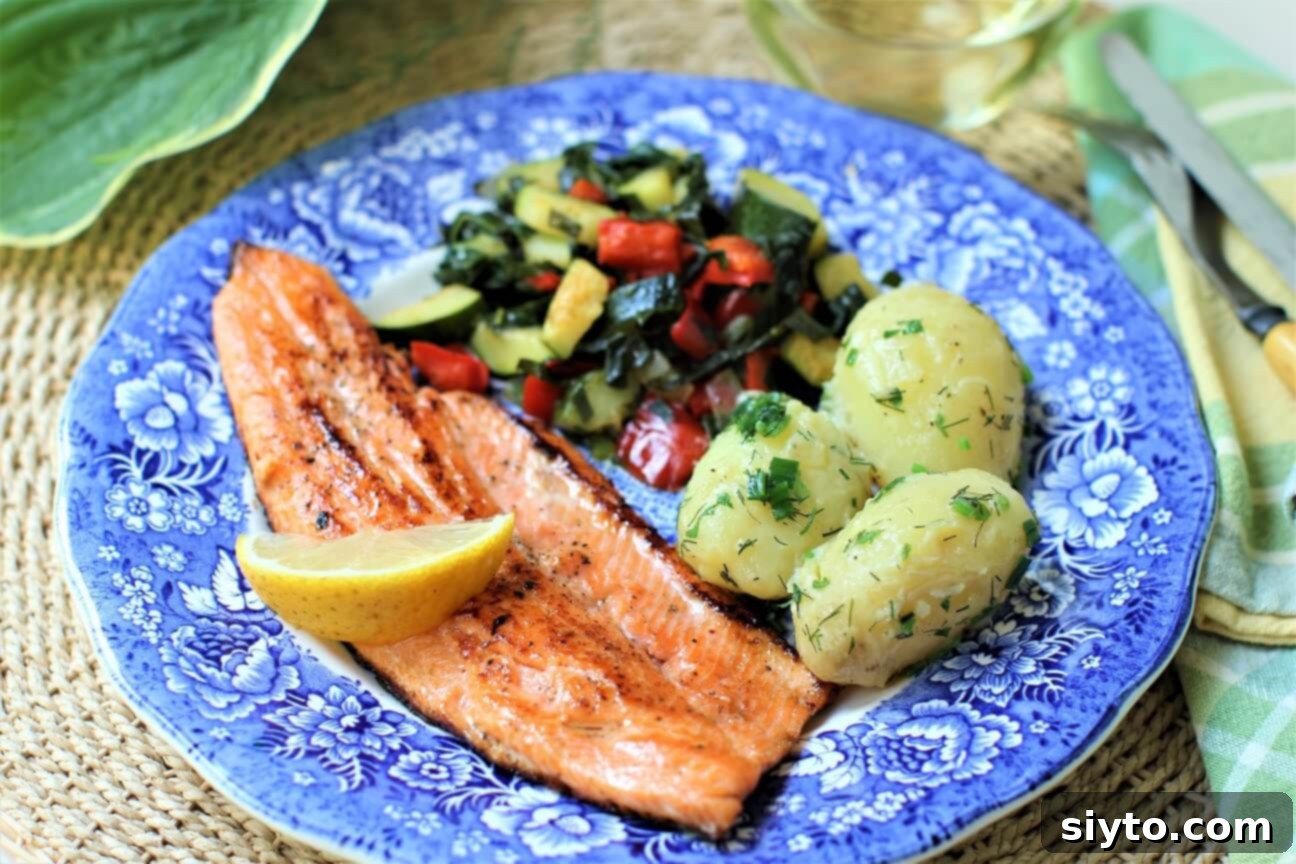 Horizontal view of a pan-fried trout fillet dinner on a blue plate, served with roasted vegetables, highlighting the golden-brown crust.