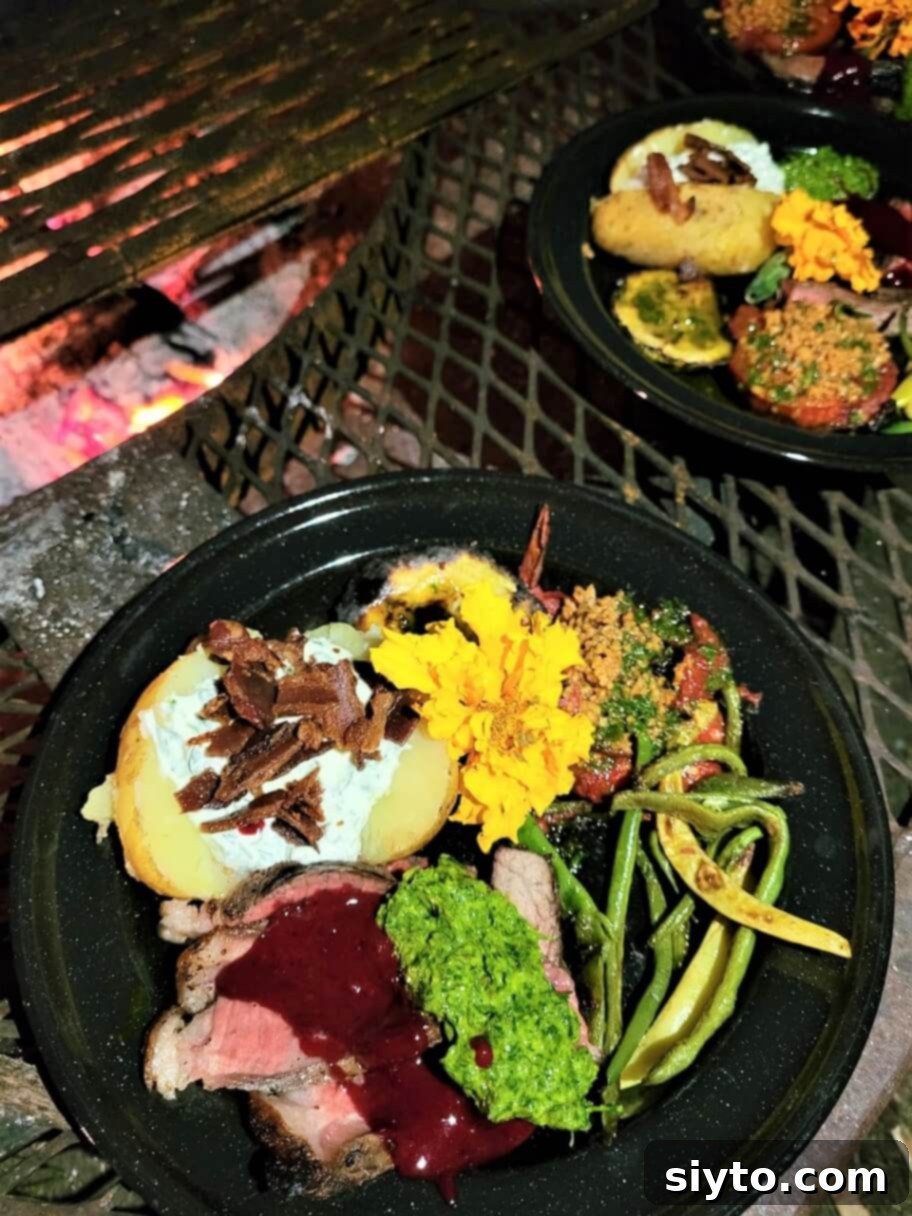 A loaded dinner plate with coal-grilled porterhouse steak, baked potato, and grilled vegetables, set beside a campfire in the evening