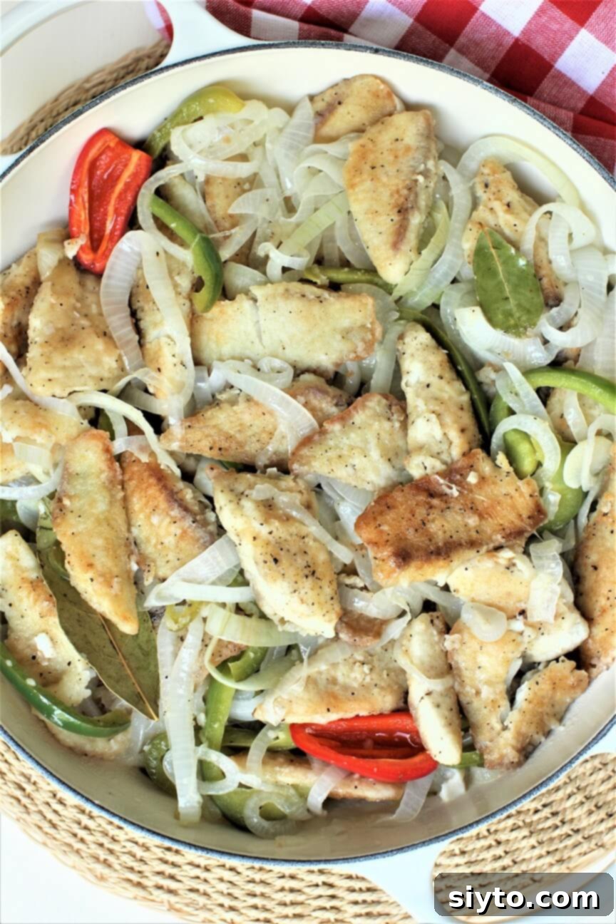 Golden-fried tilapia fillets with translucent onions, vibrant green peppers, and two red hot pepper halves, glistening with the tangy oil and vinegar sauce.