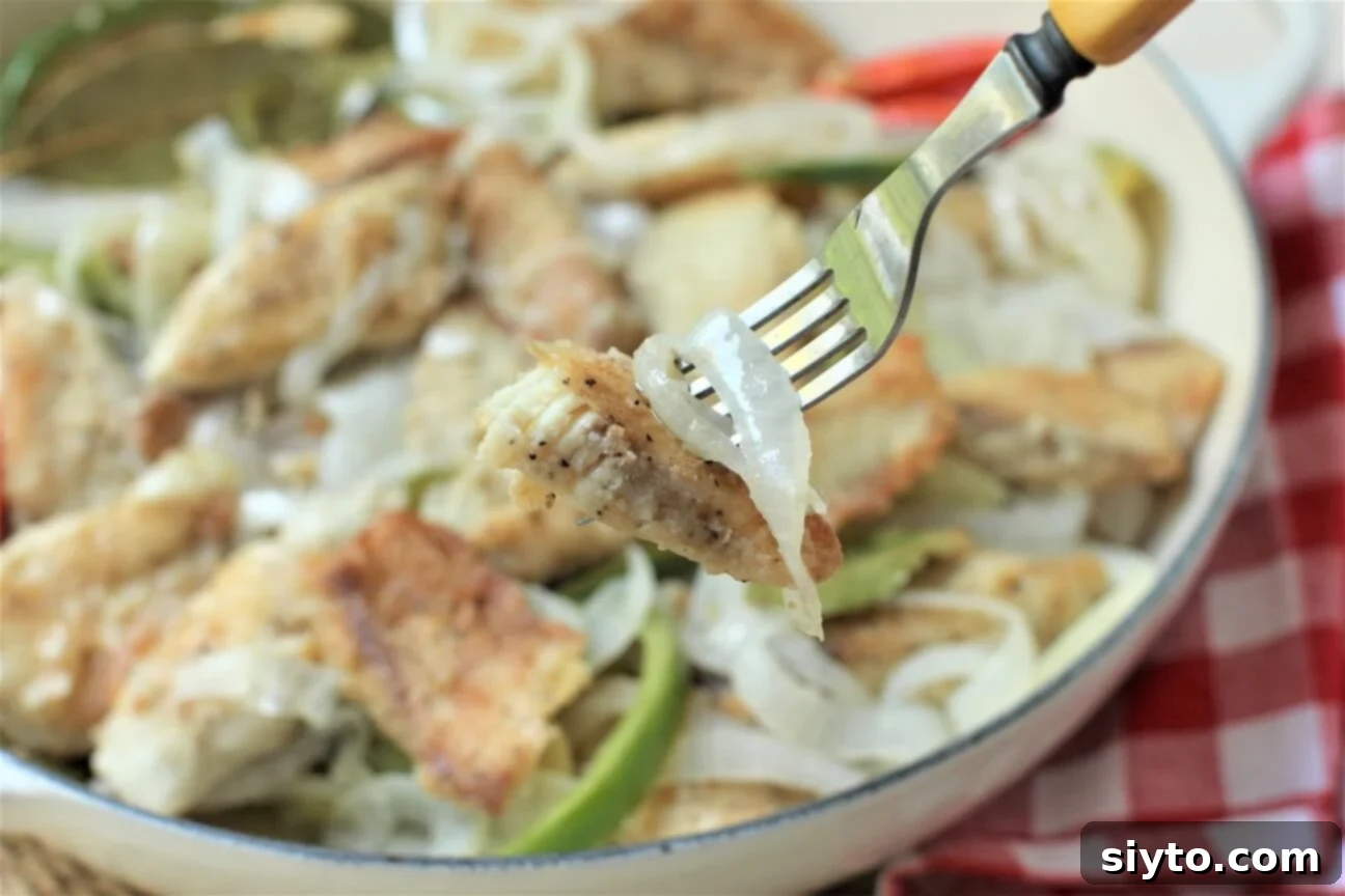 A forkful of tender, fried tilapia with onions and peppers, ready to be enjoyed.