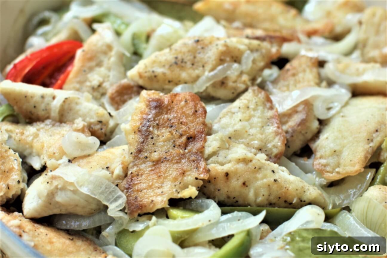 A close-up view of golden-fried tilapia fillets nestled among tender onions and vibrant peppers, glistening with the tangy oil and vinegar sauce.