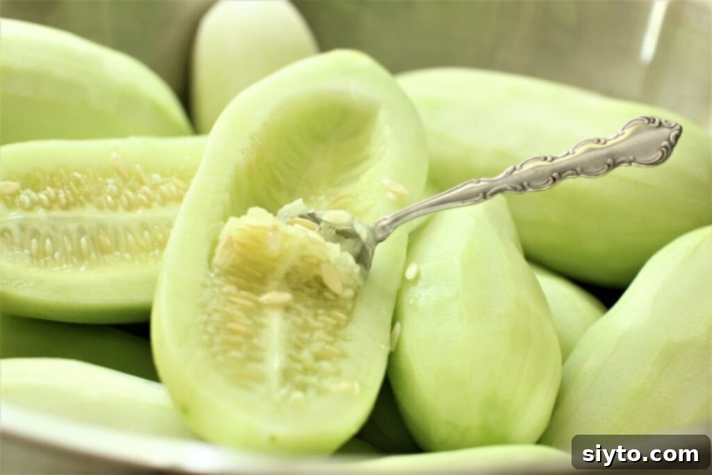 A person scooping seeds out of an overripe cucumber half with a teaspoon