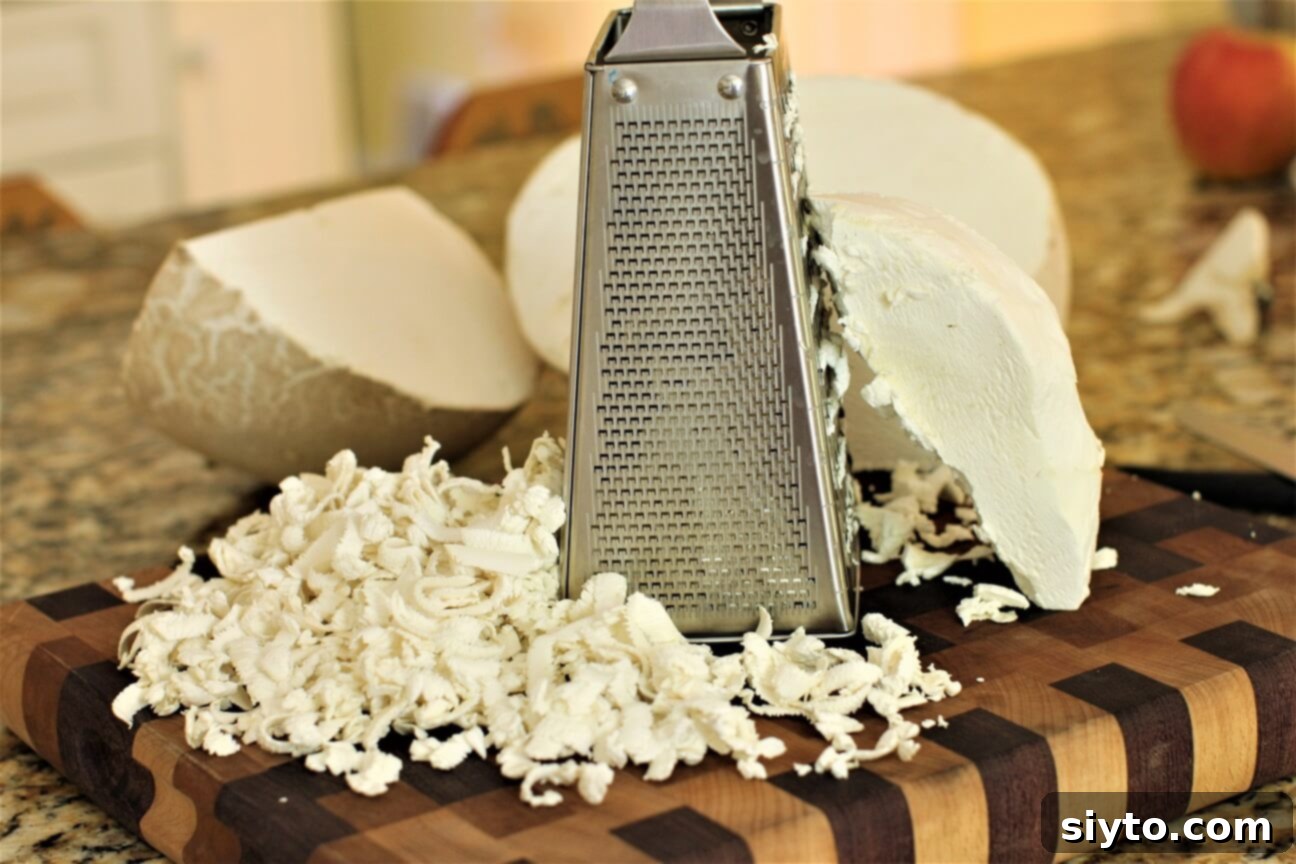 A person actively shredding a peeled giant puffball mushroom using a box grater over a bowl, illustrating the preparation process.