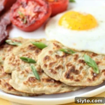 Three golden-brown boxty on a plate with fried egg, bacon, and grilled tomato