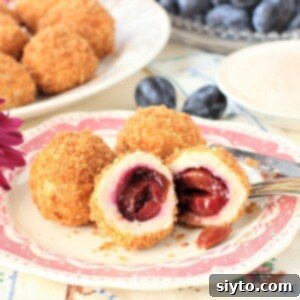 Three Hungarian plum dumplings on a pink plate, one of them is cut open to show the plum inside.