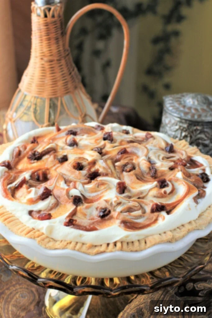 A whole Mile-High Medjool Date Caramel Apple Pie on a brown glass cake stand, showcasing its impressive height and delicious topping. This refined-sugar-free dessert features a crisp crust, tender apples, and luscious date caramel, crowned with maple-sweetened whipped cream swirls.