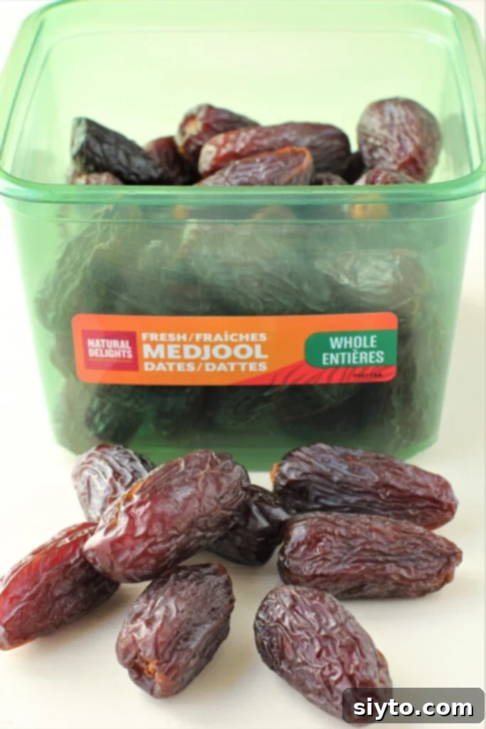 A container of Natural Delights Medjool dates with several dates scattered on a table in front, highlighting their natural and fresh appearance.