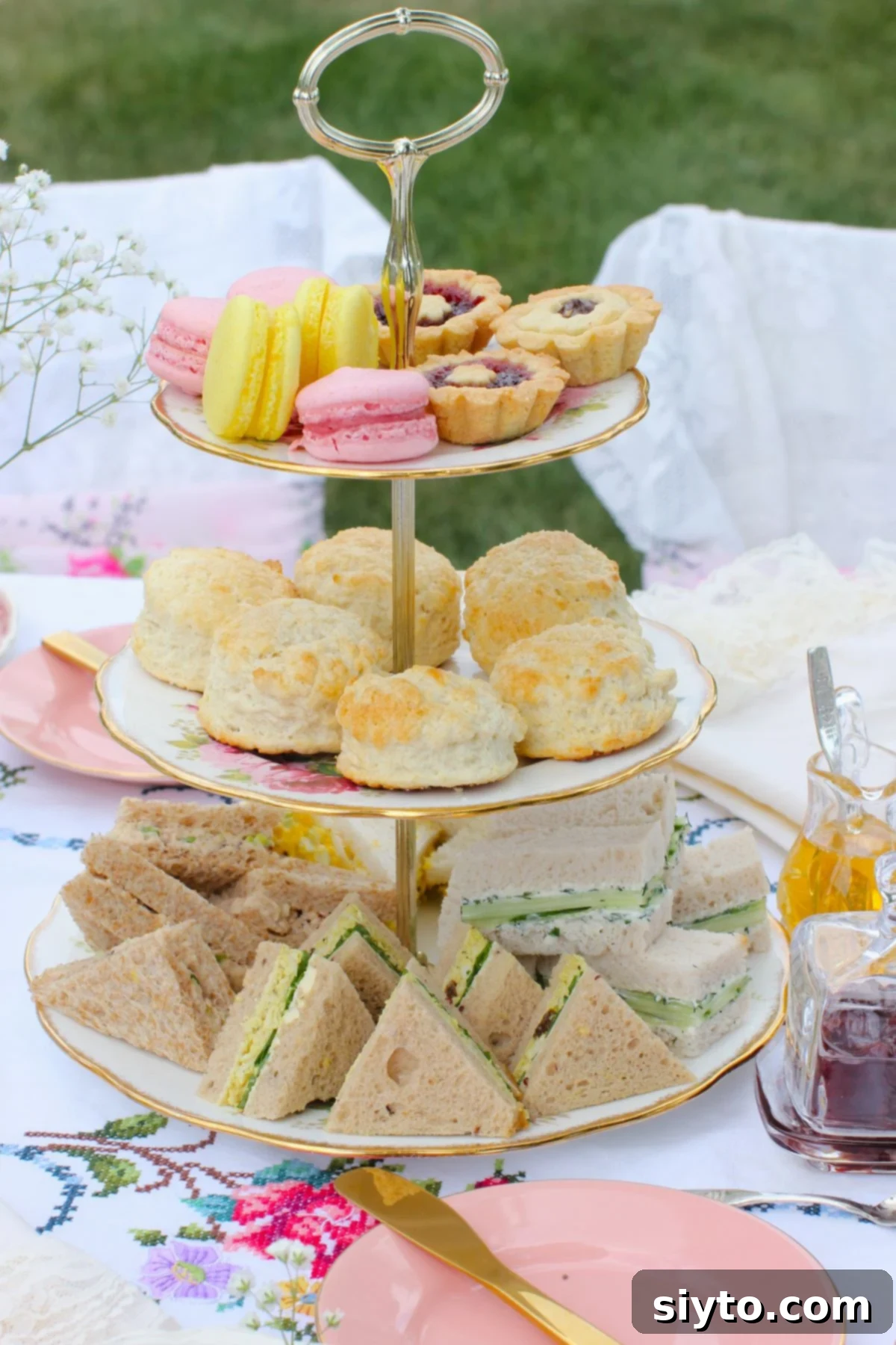 3 tier cake stand on tea table with all layers filled, sandwiches on bottom, scones in the middle, macarons and desserts on top.