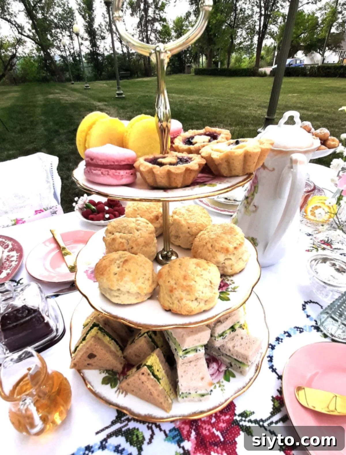 3 tier cake stand next to tall teapot, coronation chicken salad sandwiches and cucumber sandwiches on bottom tier.