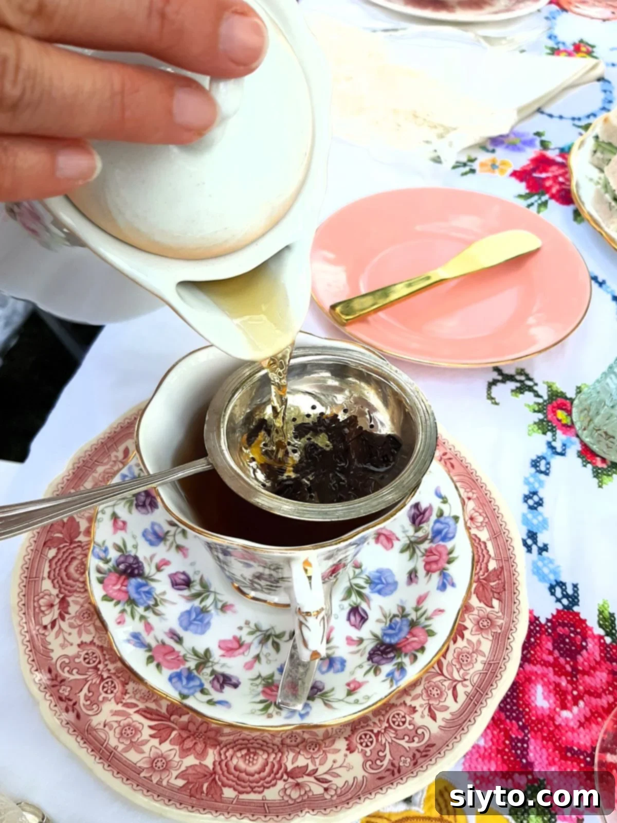 pouring Earl Grey tea through a silver tea strainer into a china cup.