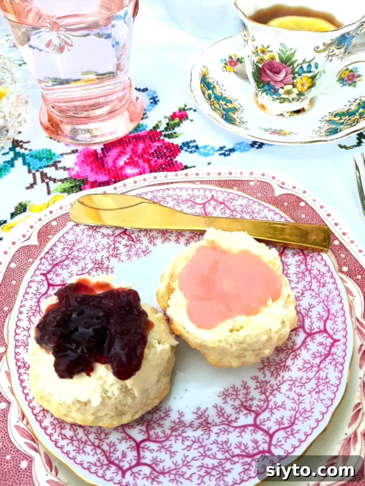 small pink and white plate with two halves of scones, one with clotted cream and jam, one with clotted cream and rhubarb curd.