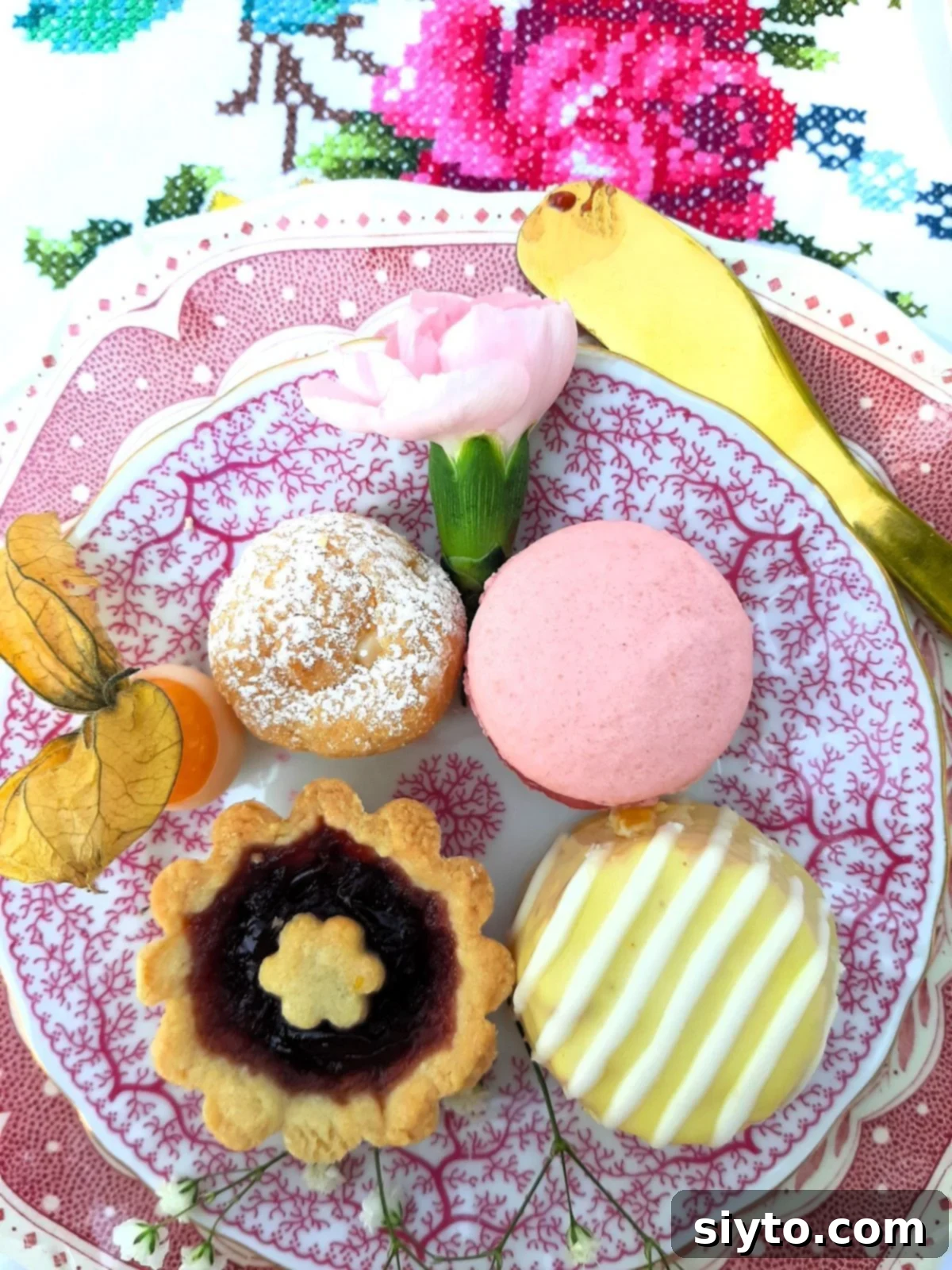 small plate with afternoon tea desserts, a profiterole, a macaron, a lemon drizzle cake, a jam crostata, and a white-chocolate dipped physalis.