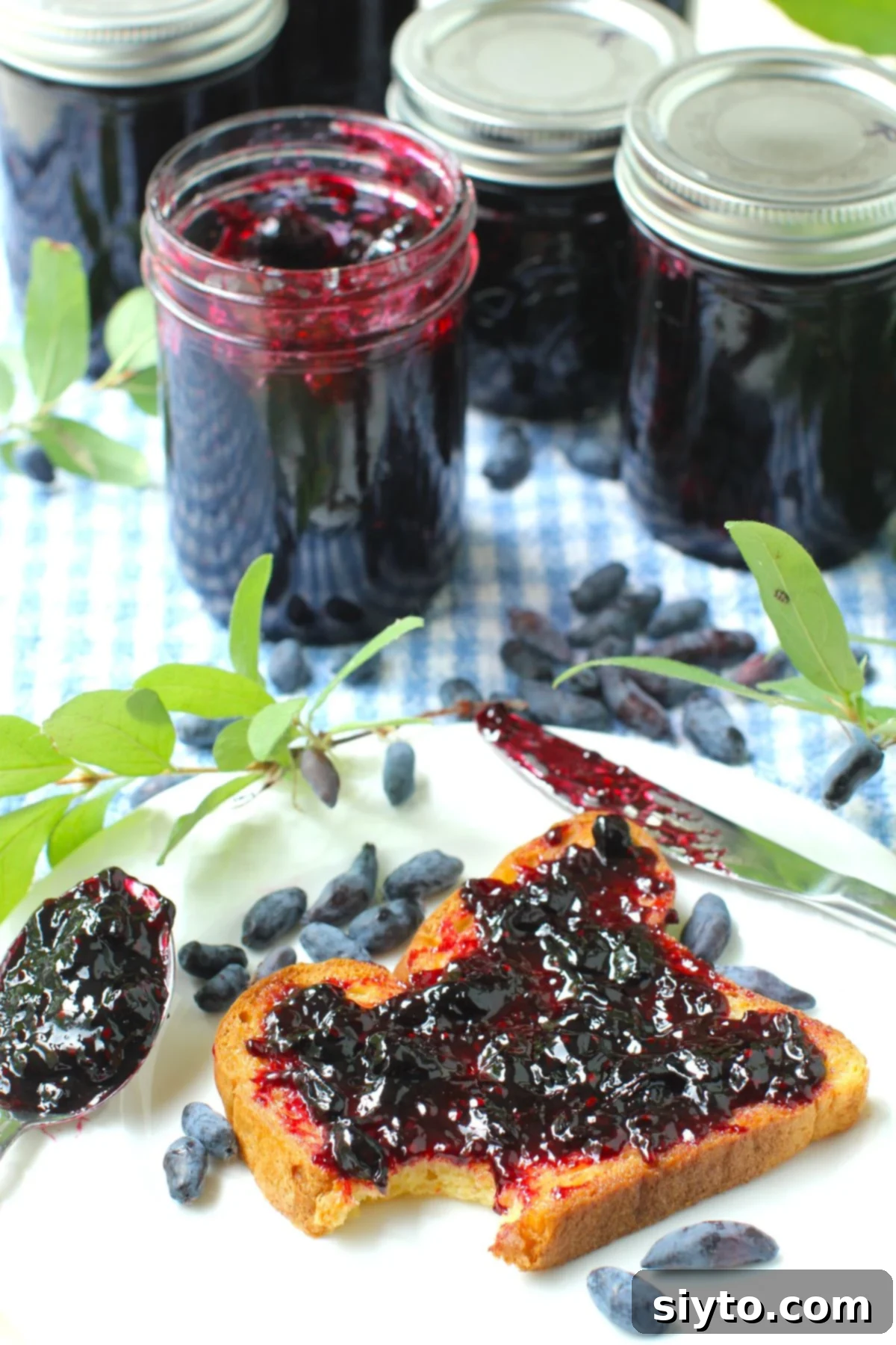 Homemade Haskap Honeyberry Jam Without Pectin 2 A slice of golden toast generously spread with homemade haskap (honeyberry) jam, with a bite taken out. Several jars of the deep purple jam are visible in the soft background.