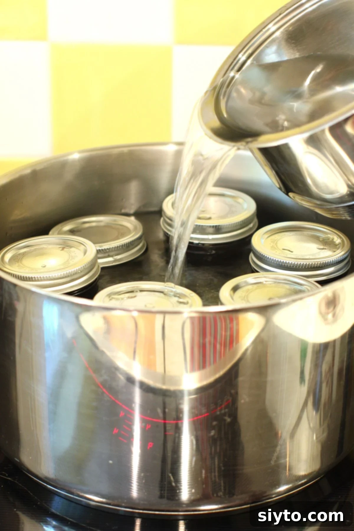 Homemade Haskap Honeyberry Jam Without Pectin 11 Water being poured into a large canning pot filled with jars of haskap (honeyberry) jam, ready for water bath processing.