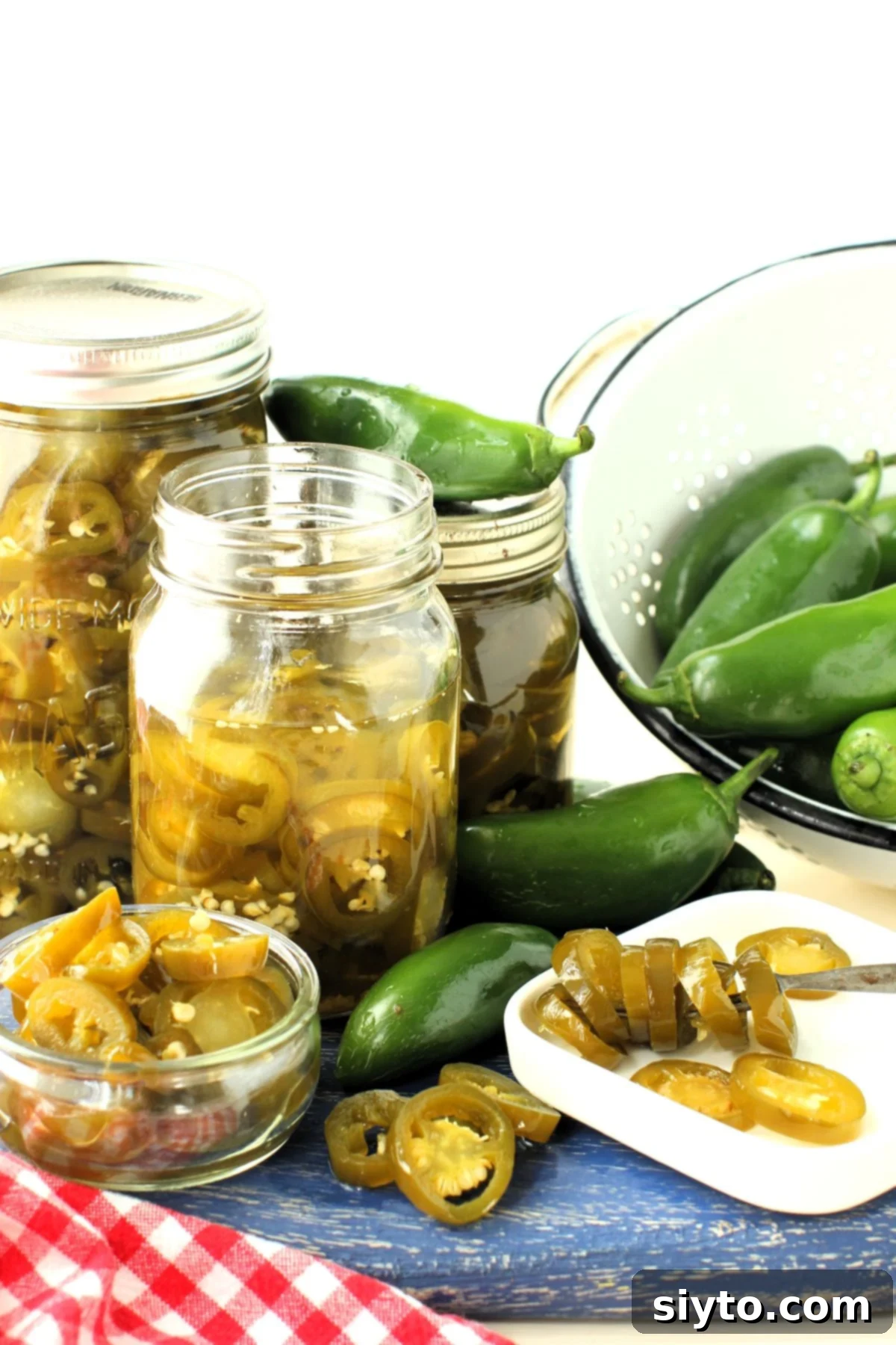 Jars of homemade candied jalapenos on a blue cutting board, with fresh jalapenos scattered around.