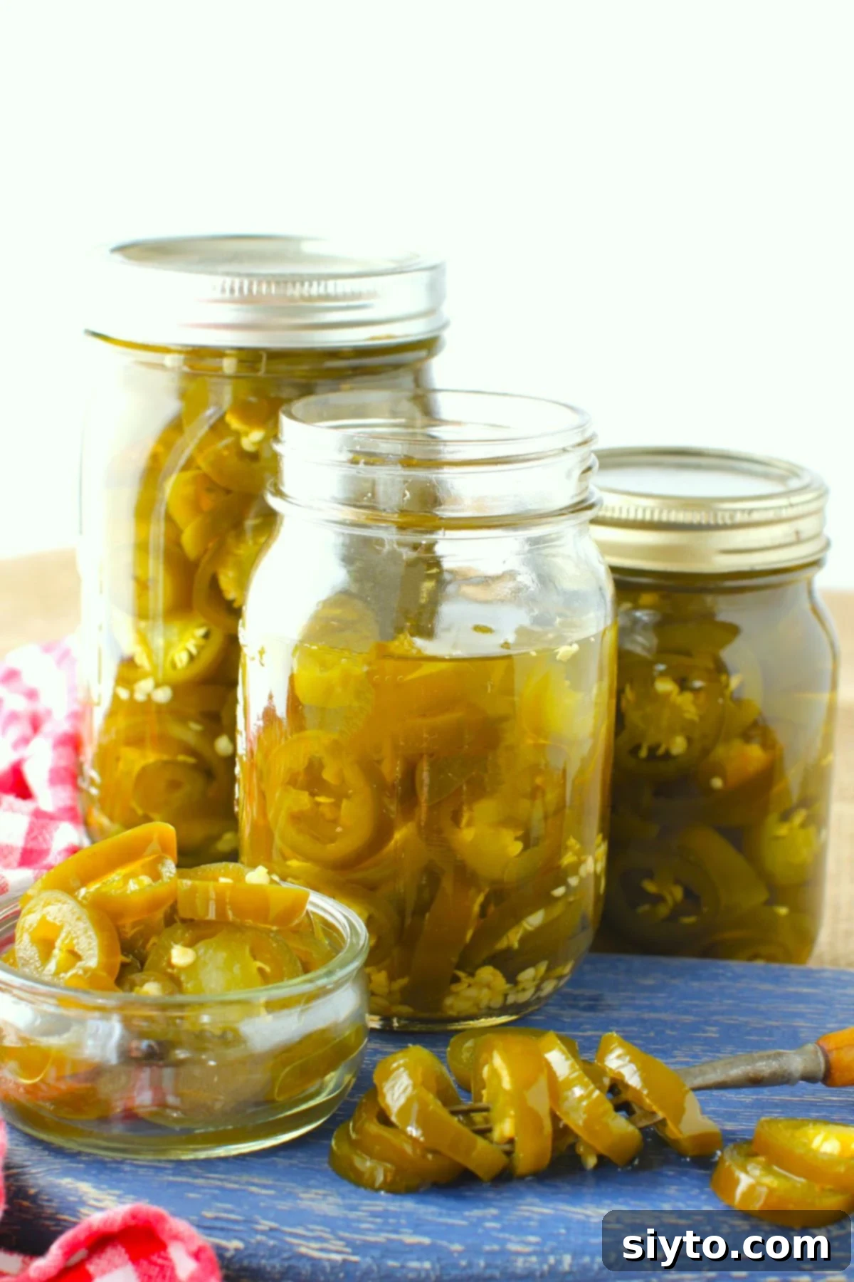 A blue cutting board featuring multiple jars of candied jalapenos, some peppers scooped onto a fork.