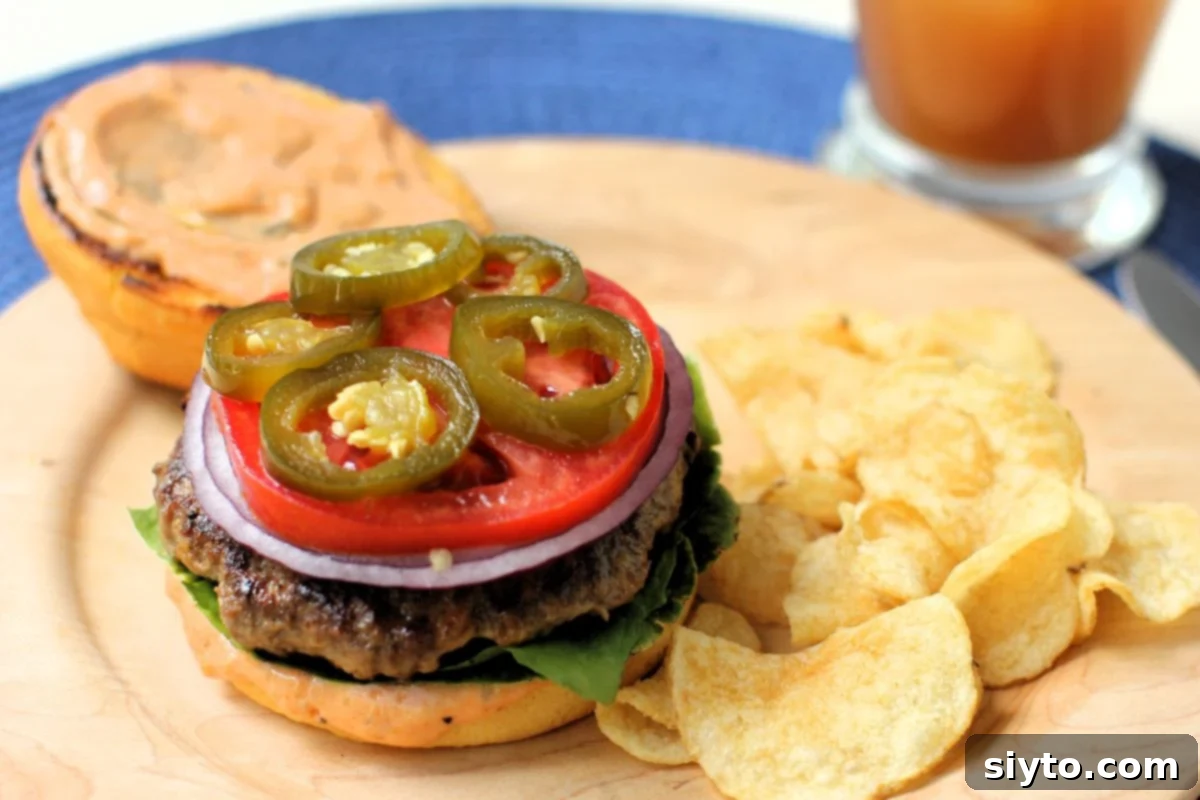 A delicious hamburger on a wooden plate with a patty, onion, tomato, and a generous topping of candied jalapenos, served with potato chips.