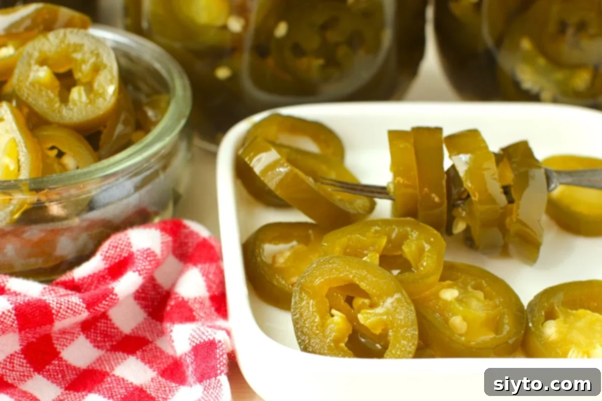 Close-up of vibrant candied jalapenos served in a small white dish, with a red and white checkered towel nearby.