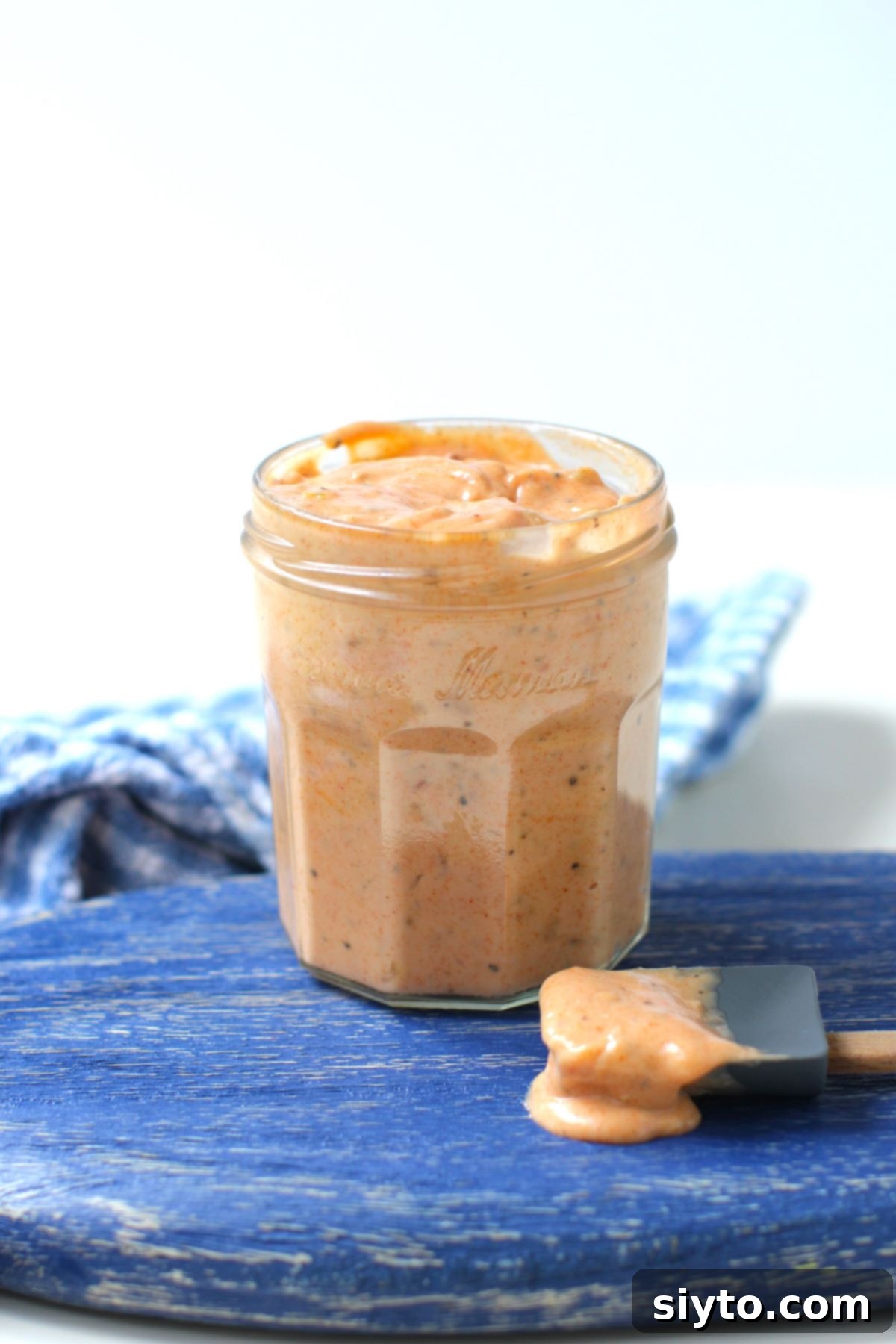 jar filled with secret Burger Sauce on a blue board, with a spoonful of sauce dripping onto board.