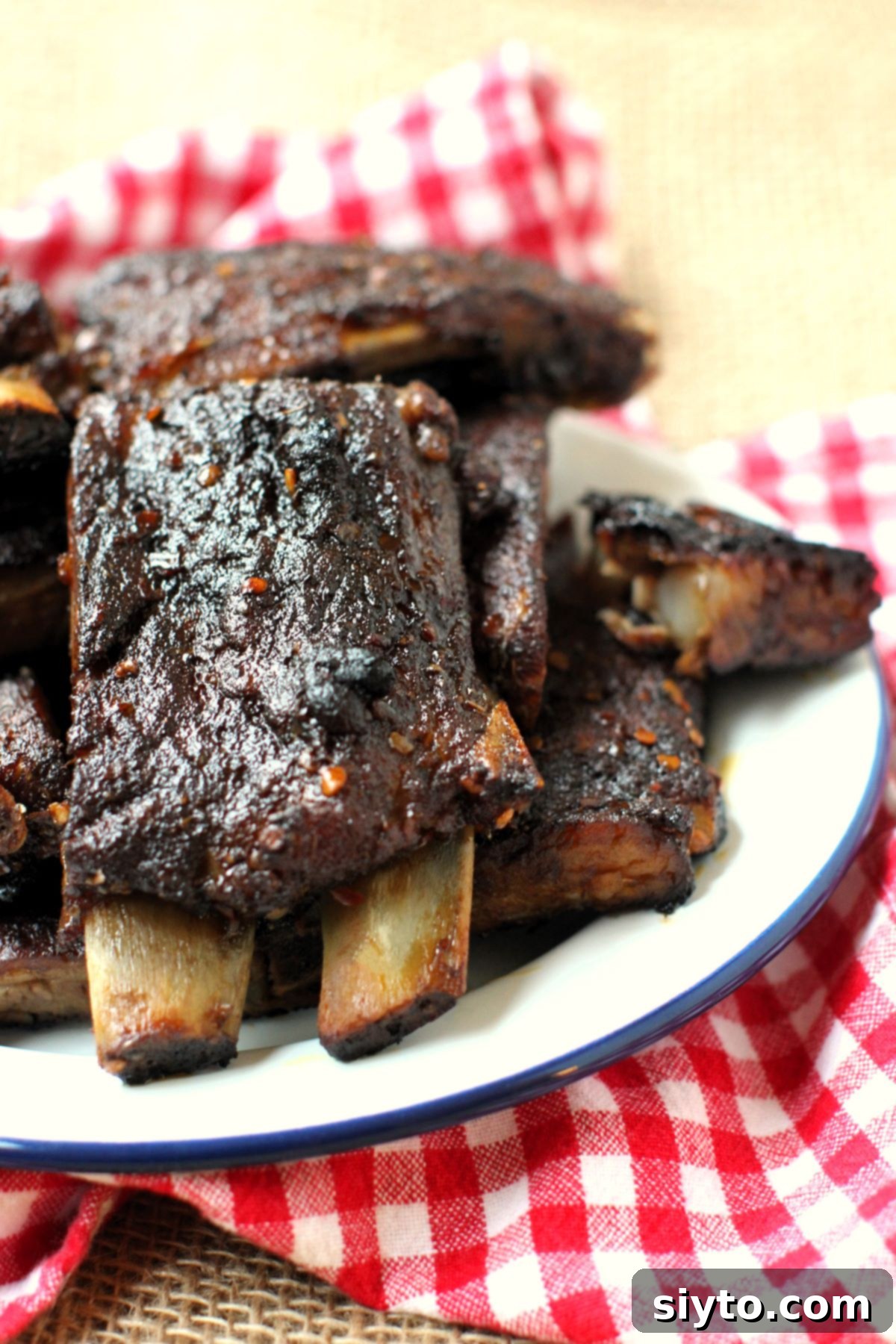 A plate brimming with expertly cooked, spicy pork ribs, cut into two-rib portions and arranged invitingly on a classic red-checked towel. The ribs glisten with a rich glaze, hinting at their sweet and spicy flavor profile.