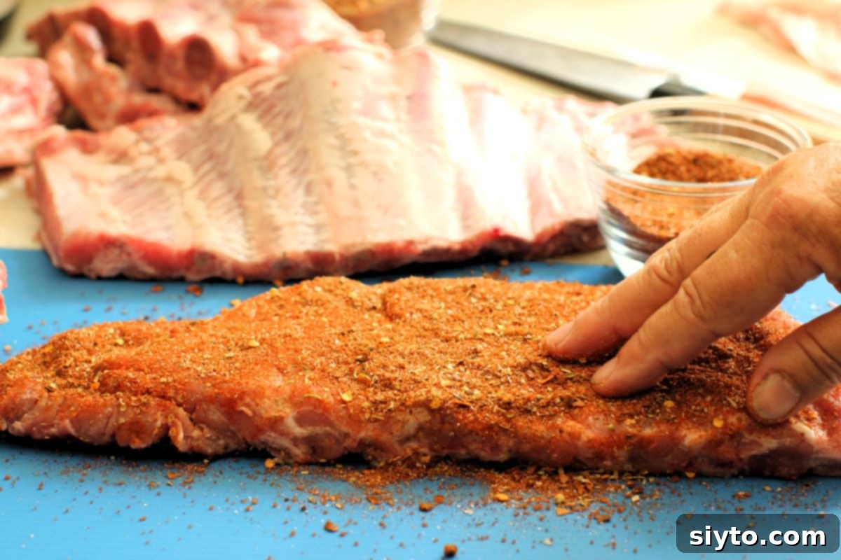 A close-up of hands thoroughly rubbing a generous amount of spicy dry rub into a rack of pork ribs, ensuring full coverage for maximum flavor.