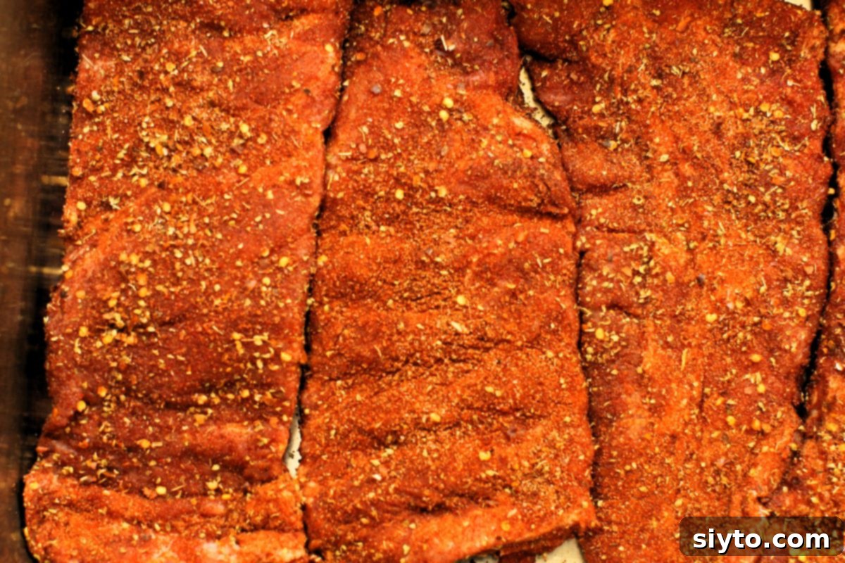 Spice-rubbed racks of pork ribs perfectly nestled in a roasting pan, covered with aluminum foil, ready for slow oven roasting.