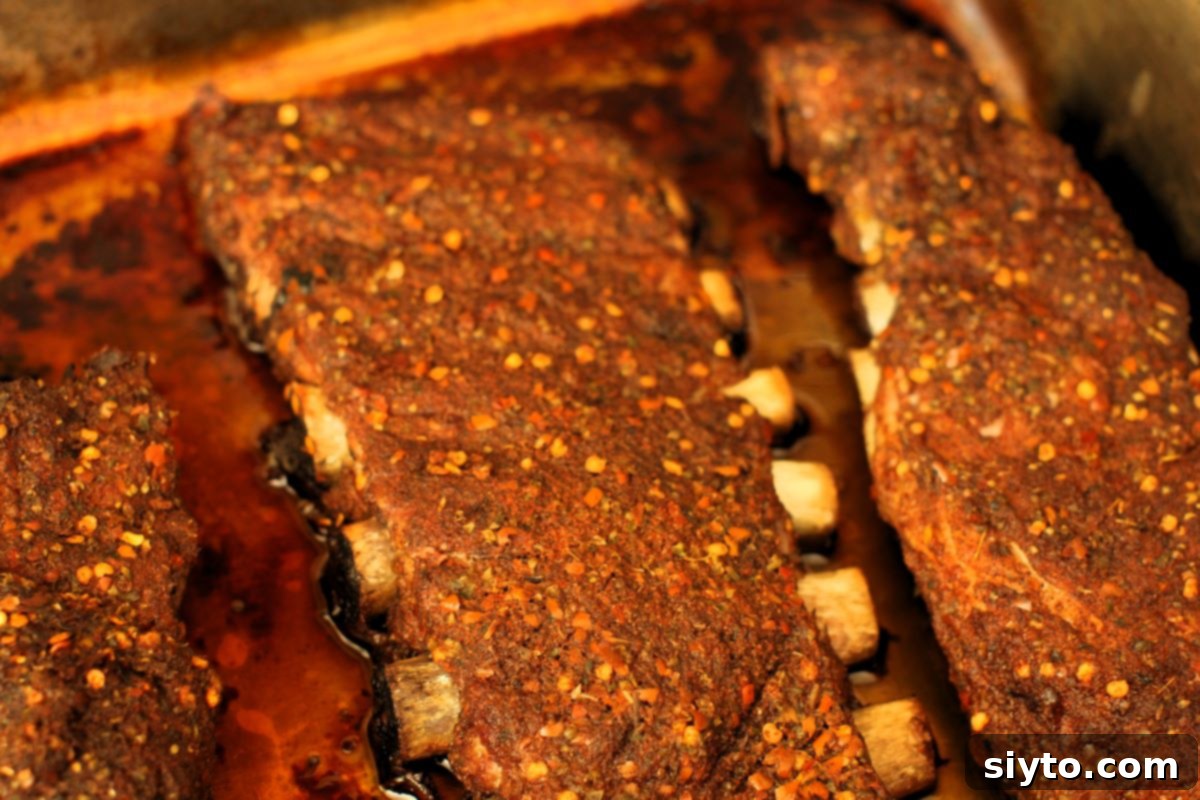Slow-roasted spicy ribs, already tender and juicy, resting in a pan, awaiting their final maple whisky glaze and finishing touch.