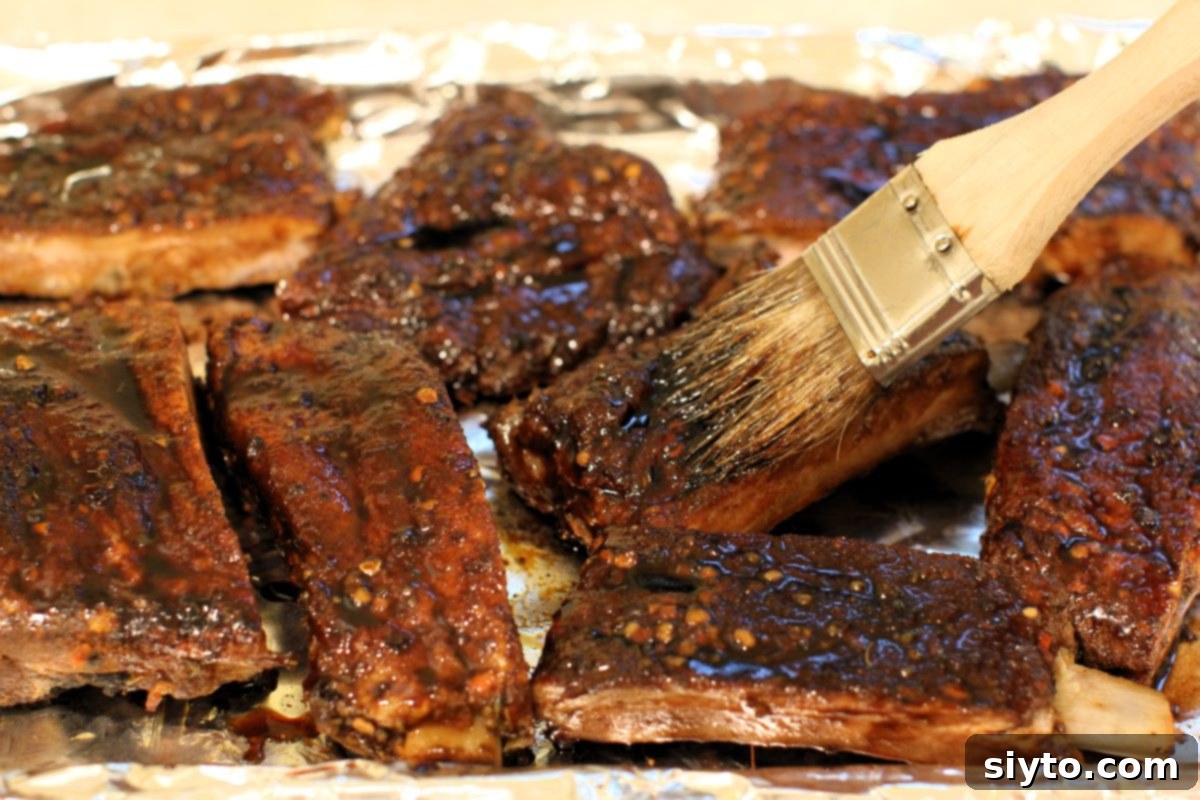 A pastry brush applying the glossy, sweet, and tangy maple whisky glaze onto the already tender spicy ribs, adding a crucial layer of flavor and caramelization.