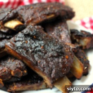 A close-up view of sticky, spicy pork ribs, perfectly cut into two-bone portions and piled high on a white plate, showcasing their rich glaze and tender texture.
