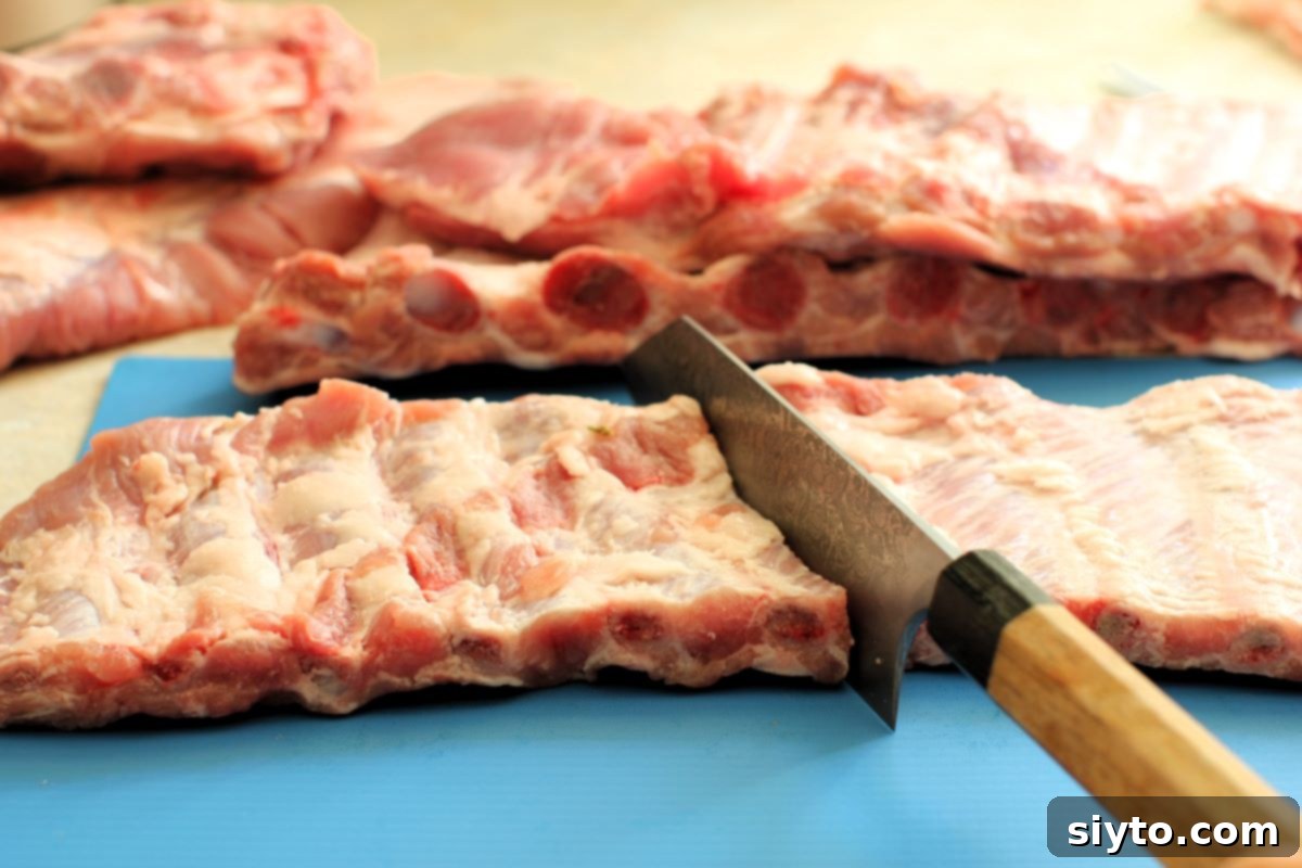 A hand skillfully cutting a full rack of pork ribs in half, demonstrating a practical step for preparing ribs for roasting or grilling.
