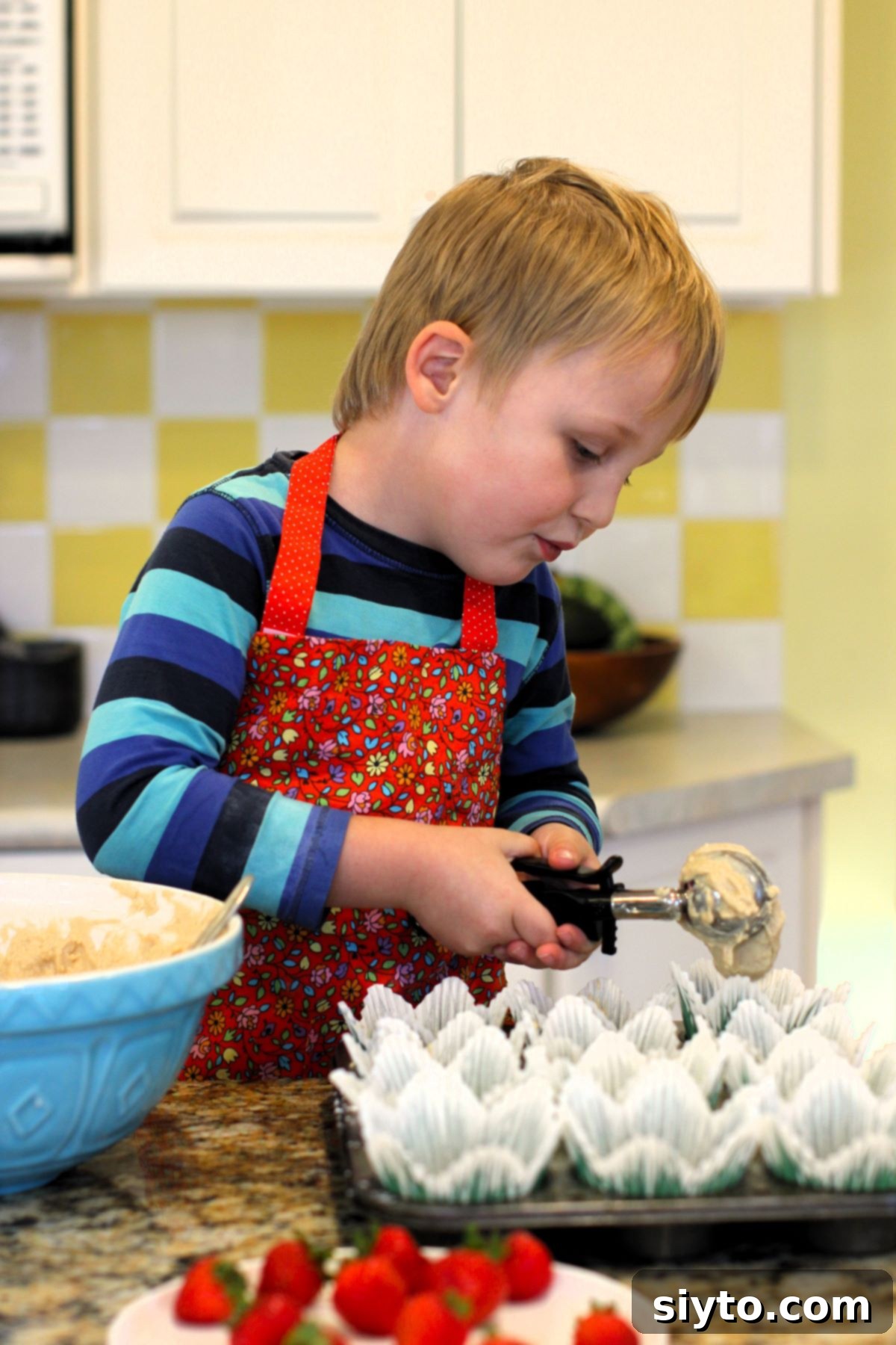 Caleb using the ice cream scoop to fill the muffin papers.