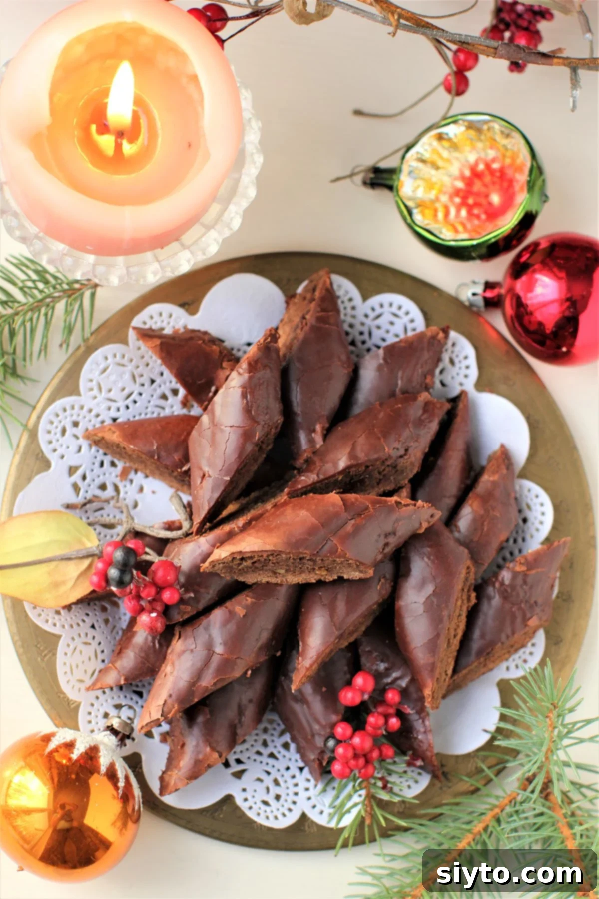 top-down view of a plate of Magenbrot diamonds on a lace doily on a plate with Christmas balls around, and a candle burning in the top left corner.