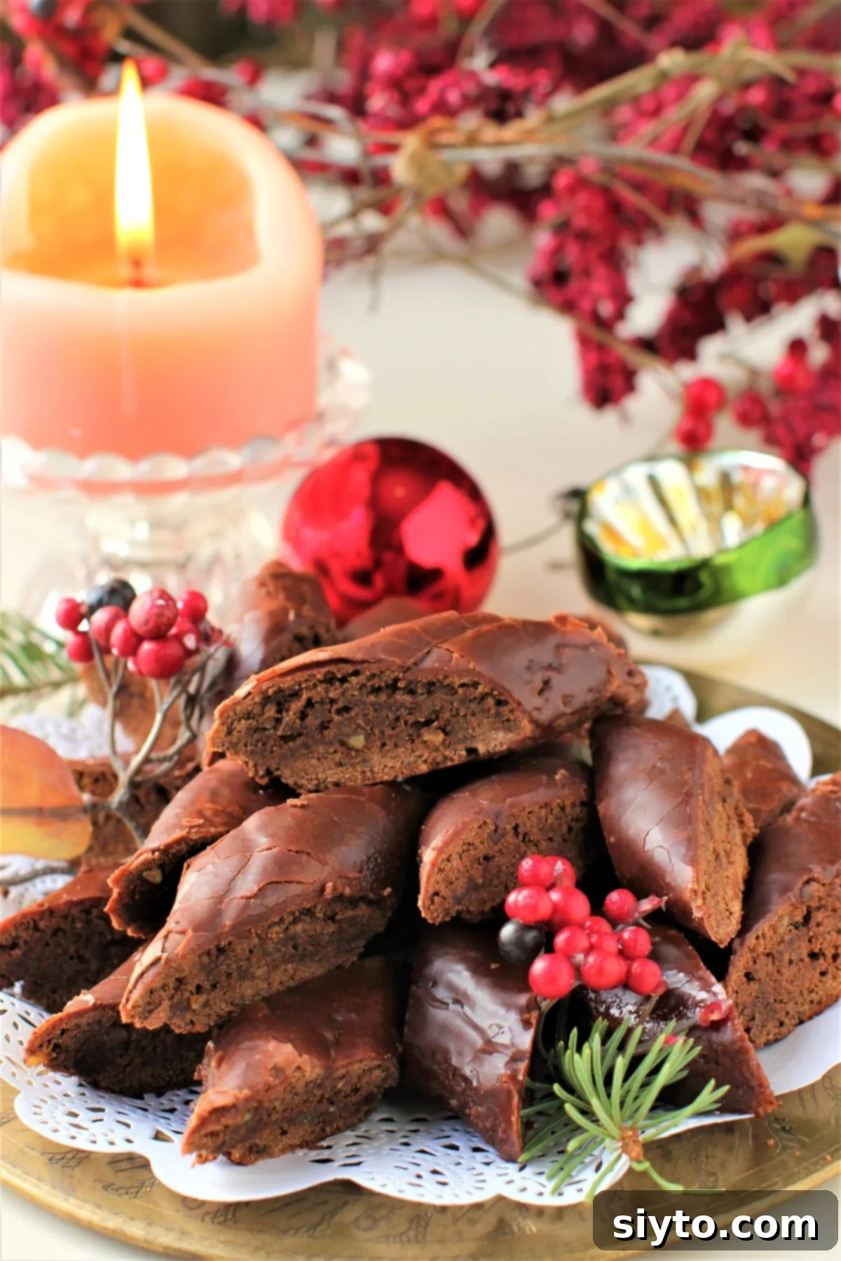 plate of German Magenbrot glowing in front of a lit candle and red berries in the background.