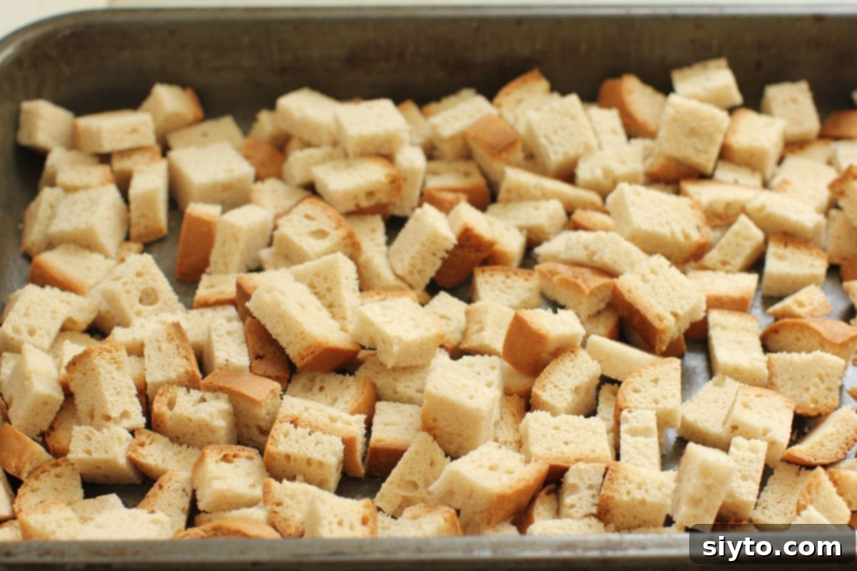An overhead shot of a baking pan filled with evenly spread bread cubes, air-drying to achieve the perfect texture for stuffing.