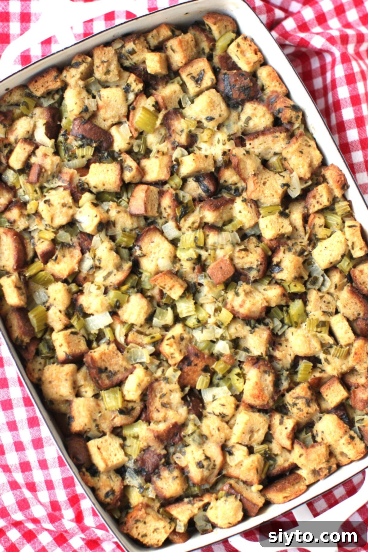 A top-down view of a rectangular white baking pan brimming with freshly baked gluten-free stuffing, just out of the oven, showing a golden crust and inviting texture.