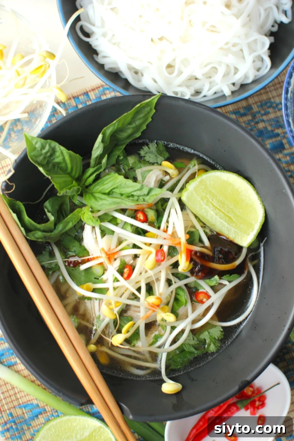 a black ceramic bowl of easy chicken pho soup with a bowl of cooked rice noodles beside it.