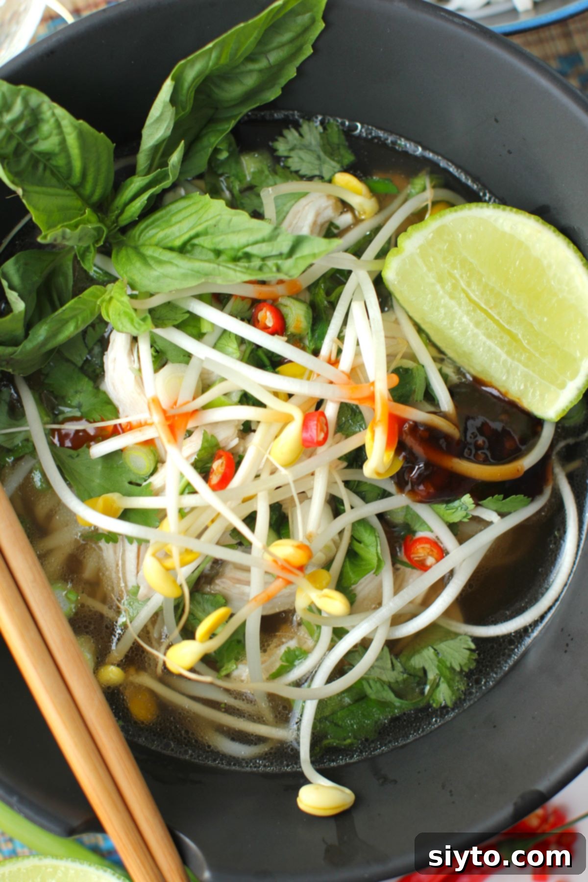 pho soup in a black bowl, with lime wedge and basil.