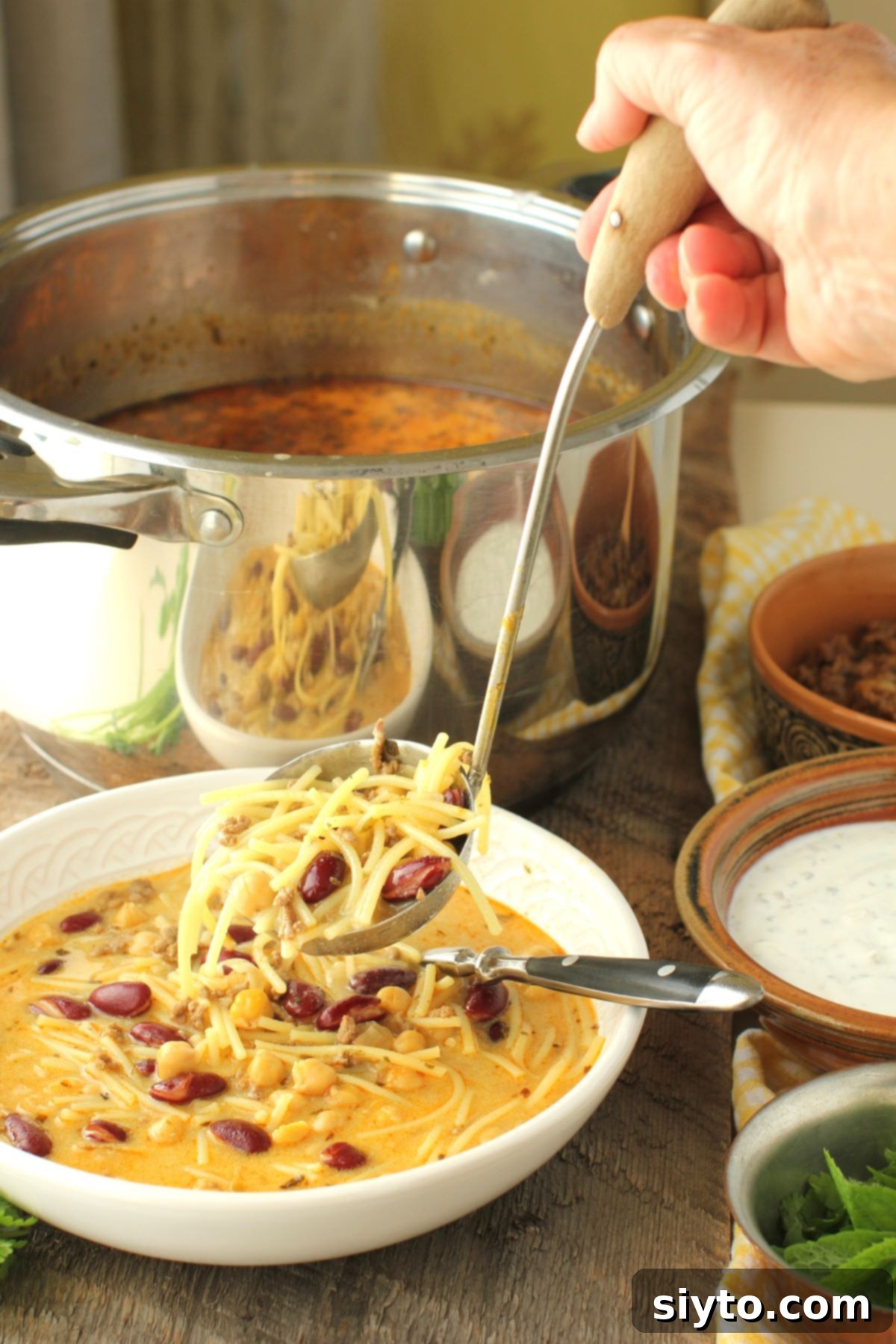 A close-up shot of a hand gracefully ladling a serving of Aush noodles and beans into a pristine white bowl, highlighting the hearty components of the Afghan noodle soup.