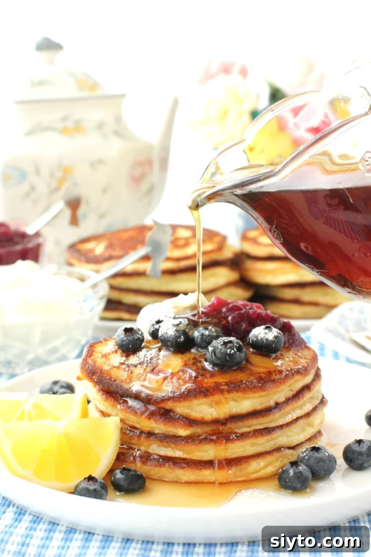 Fluffy Lemon Ricotta Pancakes 2 Pouring syrup onto the pancake stack, with teapot and more pancake stacks in the background.