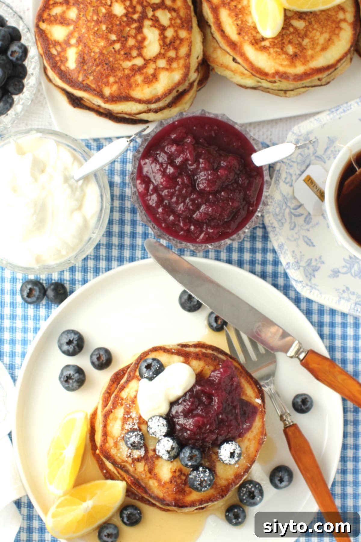 Fluffy Lemon Ricotta Pancakes 8 Top-down view of breakfast table with lemon ricotta pancakes on plate, bowls of blueberries, yogurt, and blueberry applesauce, plate of pancake stacks.