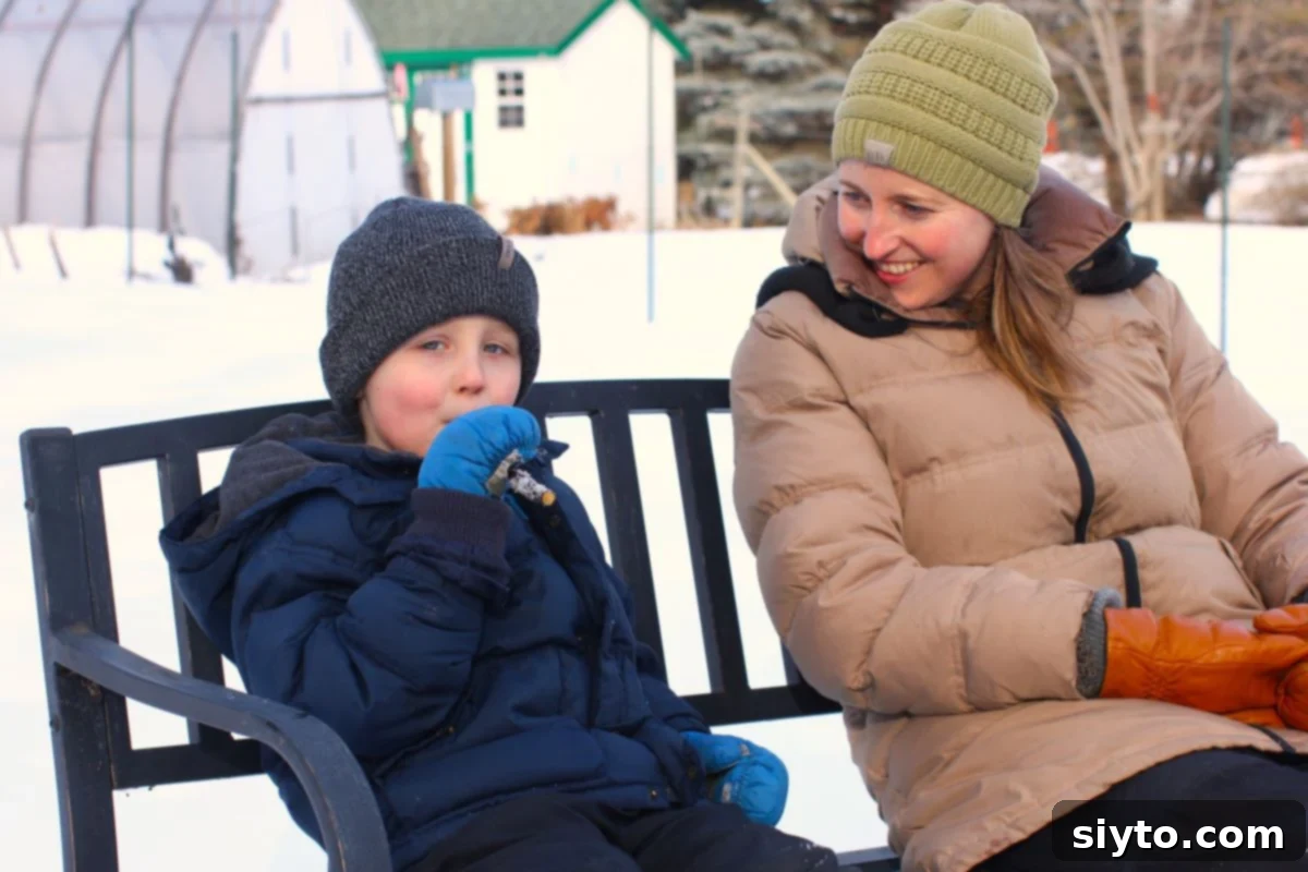 Oschean and Caleb sitting on an outdoor bench. Caleb is happily enjoying his maple snow candy.