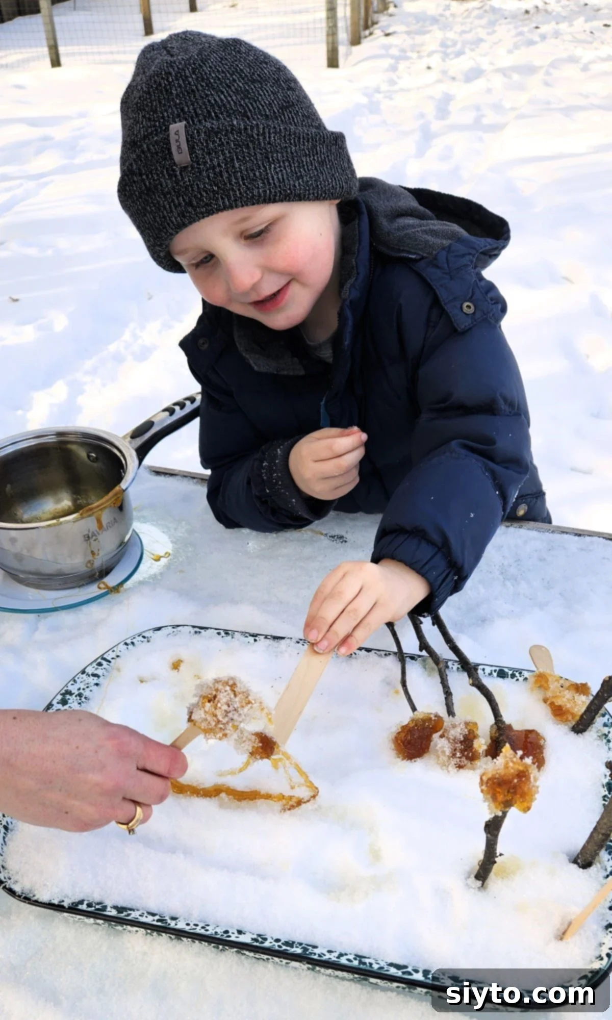 Caleb and another child, O., actively rolling up the sticky maple syrup from the snow onto their sticks.