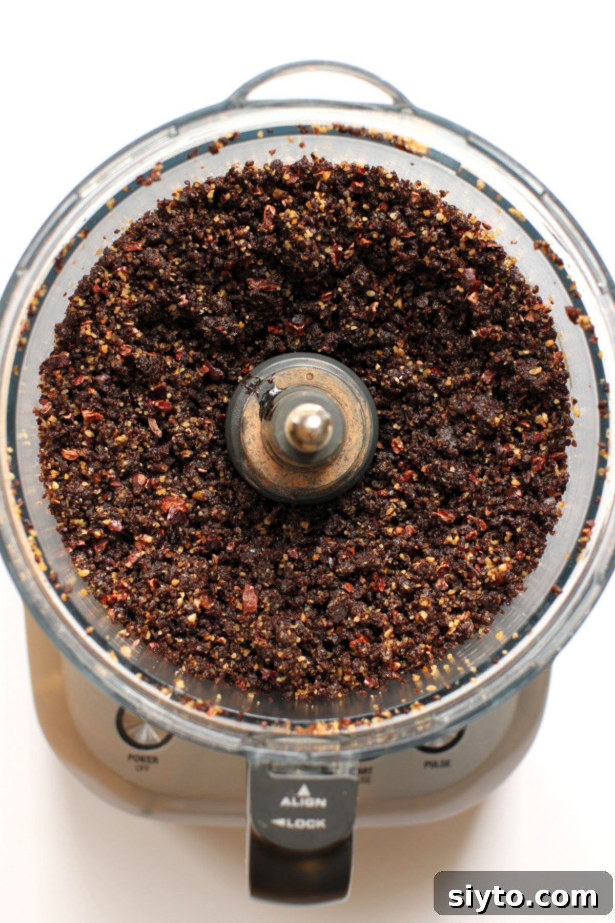 Sweet Bites Snowy Sleds: Lake Louise Adventures 15 A top-down view into the bowl of a food processor, showing a crumbly, well-mixed dark brown mixture, indicating the readiness of the licorice ball dough.